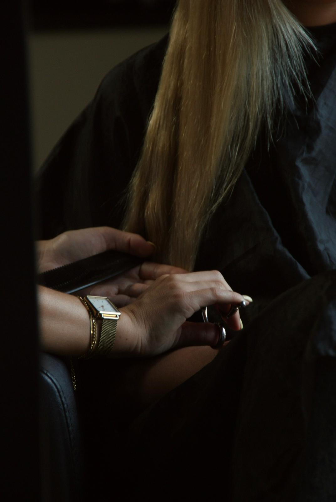 Handen aan het werk in blond haar onder een kapmantel, in een donkere salonhoek