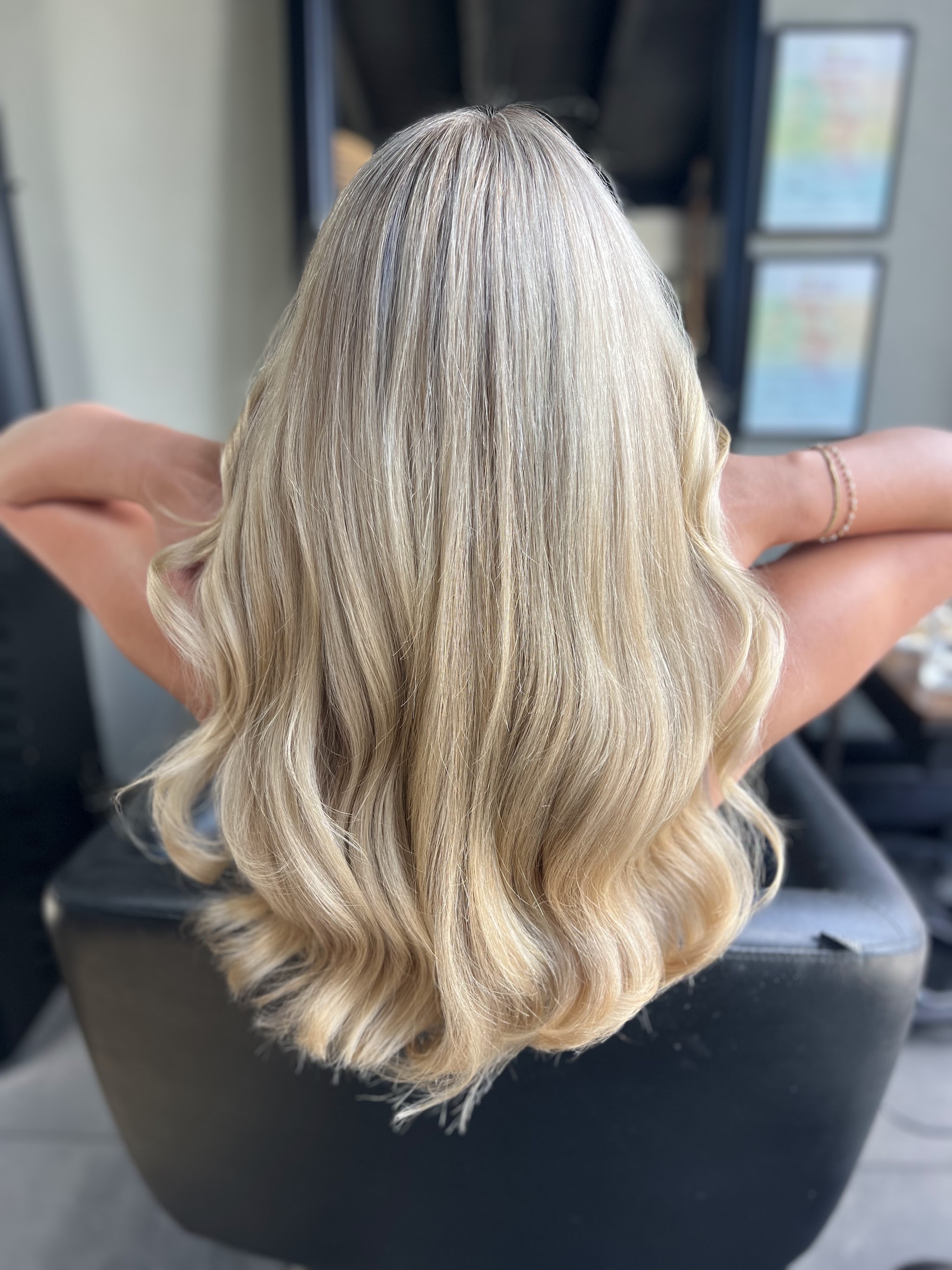 Lang blond haar met balayage in zachte golven, van achteren gezien in de salonstoel