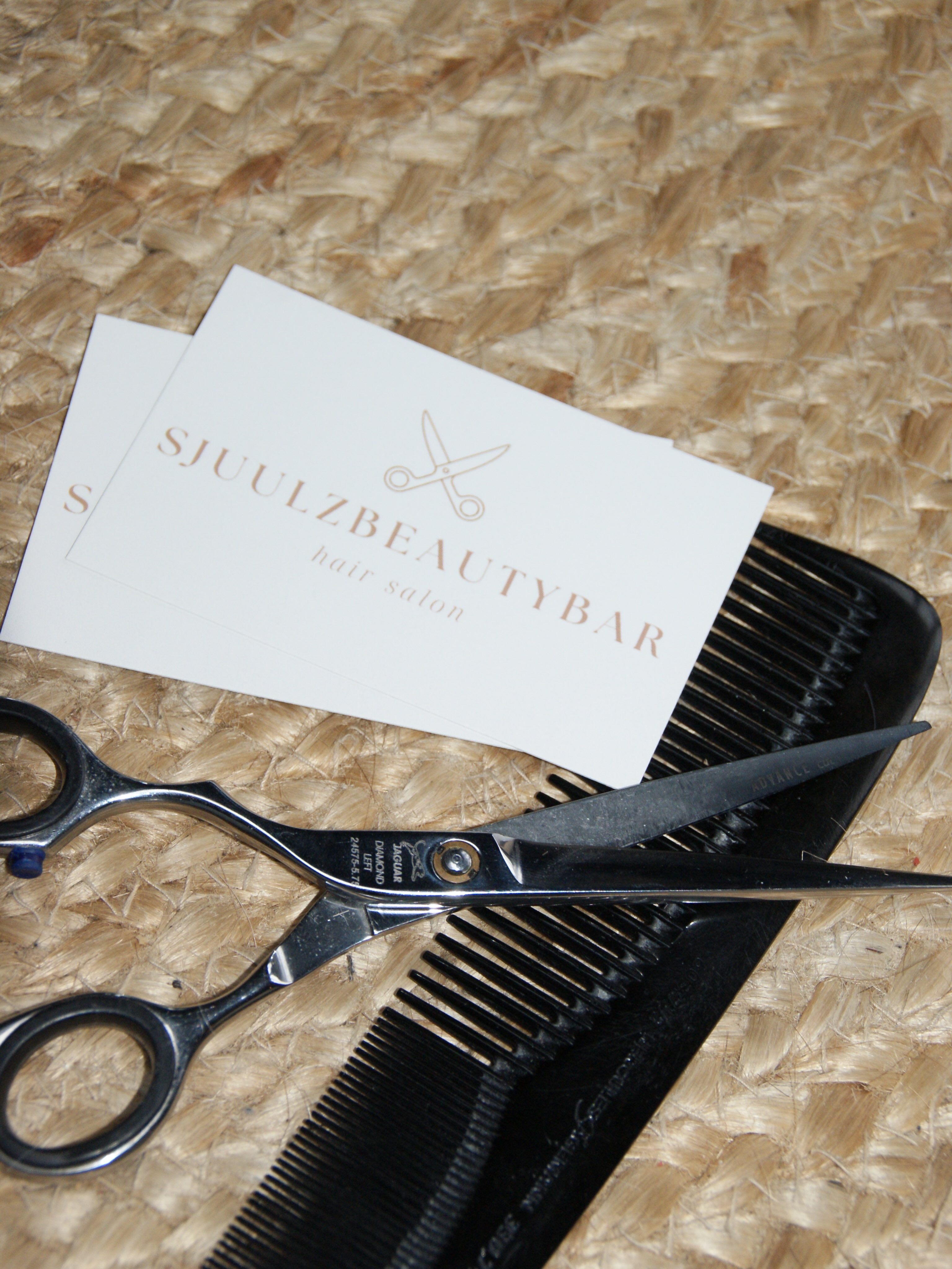 Visitekaartjes van SjuulzBeautyBar met een schaar en een kam op een jute mat